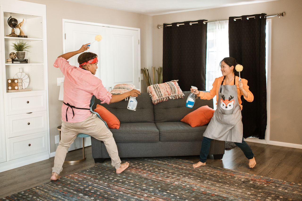 A cheerful couple is caught in a playful cleaning tussle in their living room, highlighting the fun side of everyday home life.