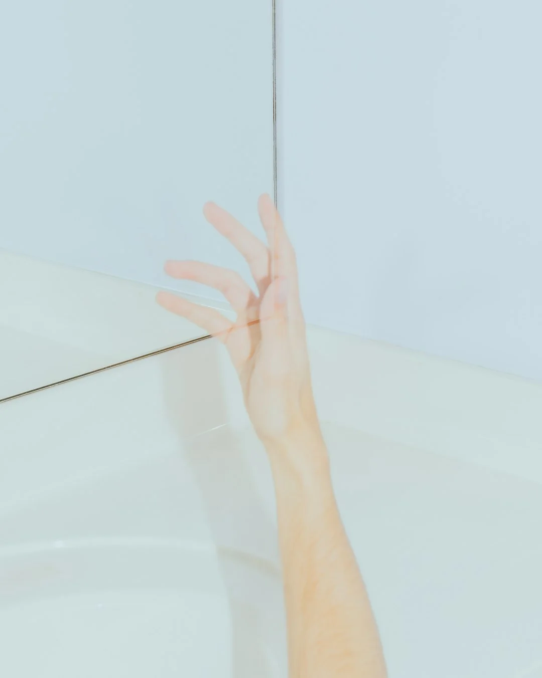 Une femme nettoie un miroir à l’intérieur avec un chiffon bleu, évoquant la propreté et l’entretien de la maison.